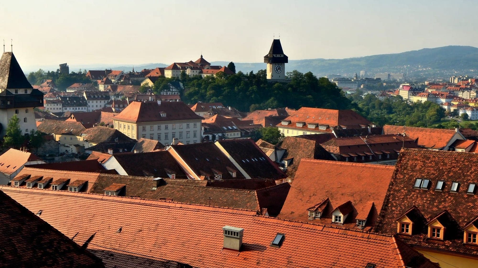 View across the red roofs of Graz old town to the clock tower on the Schlossberg in evening light
